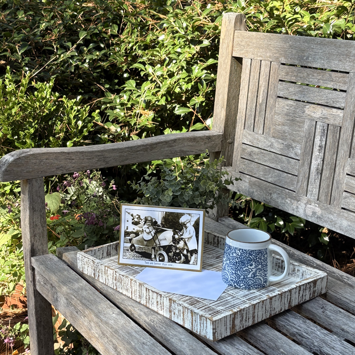 A greeting card and coffee mug sitting atop a wooden bench.